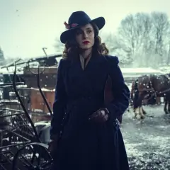 Elegancka kobieta w kapeluszu i płaszczu, w zimowej scenerii, jak z filmu Peaky Blinders.