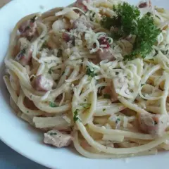 Pyszna, kremowa wloska carbonara z kawałkami boczku i posypana parmezanem, udekorowana natką pietruszki.