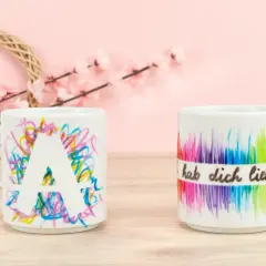 Kreative tassen bemalen ideen: eine Tasse mit dem Buchstaben A und bunte Kritzeleien, daneben eine Tasse mit Regenbogenfarben und der Aufschrift "hab dich lieb".