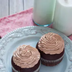 Deux cupcakes au chocolat avec une ganache chocolat passion onctueuse, servis sur une assiette bleue avec deux verres de lait.