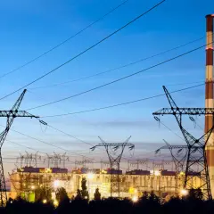 Elektrownia z kominem i liniami wysokiego napięcia. W tle widać budynki zakładu, a nad nimi niebo o zmierzchu. To obraz, który może kojarzyć się z opłatą kogeneracyjną.