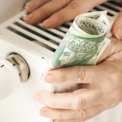Ręce trzymają banknot 100 zł przy grzejniku. Sprawdzanie rachunków za ogrzewanie, cennik pogotowia gazowego.