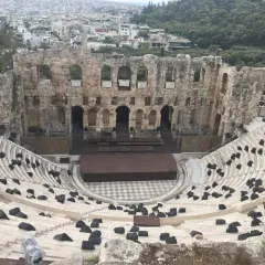 Starożytny Odeon Heroda Attyka w Atenach, z kamiennymi siedzeniami i sceną, w tle widać miasto.
