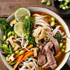 En skål med pho recept med nudlar, biff, grönsaker och lime.