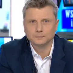 Rafał Wojda, wiek dziennikarza widoczny w jego spojrzeniu, w garniturze przed ekranem z napisem "Wstajesz i wiesz".