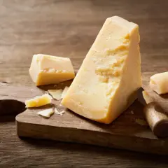 Kawałki parmezanu na drewnianej desce z nożem do sera.