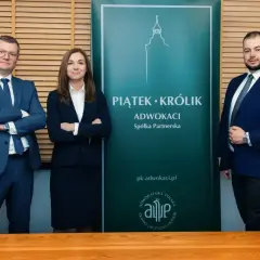 Trzy osoby w garniturach stoją przed zielonym banerem kancelarii "Piątek • Królik Adwokaci".