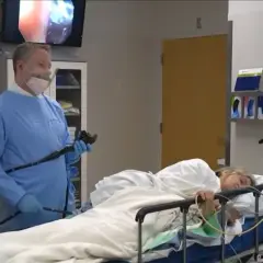 Lekarz przygotowuje się do kolonoskopii w znieczuleniu ogólnym. Pacjentka leży na łóżku, monitorowana przez sprzęt medyczny.
