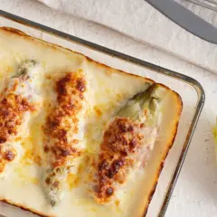 Endivias a la plancha con jamón, gratinadas con queso y bechamel en una fuente de cristal.