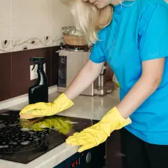 Mujer con guantes amarillos limpiando la placa de inducción con espuma.