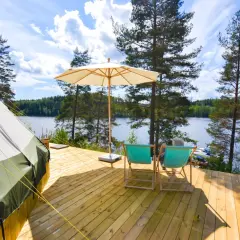 En glampingtält och två solstolar på en träaltan vid en sjö. En perfekt plats att koppla av på Råå Vallar Resort.