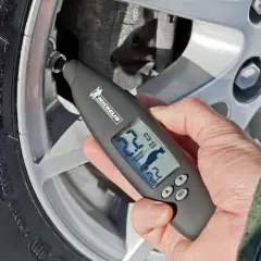 Mano usa un medidor digital Michelin para comprobar la **pegatina presión neumáticos** de un coche.