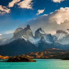 Majestatyczne szczyty Torres del Paine w **Tierra del Fuego** oświetlone słońcem, z turkusowym jeziorem u podnóża.