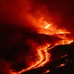 Glühende Lava fließt den Hang eines Vulkans auf Sizilien hinab, umgeben von Rauch und Dunkelheit.