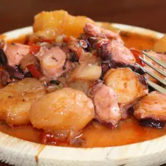 Pulpo a la mugardesa, un plato gallego con trozos de pulpo tierno y patatas cocidas en una salsa rojiza.
