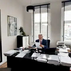 Adwokat w garniturze siedzi przy biurku w biurze, przeglądając dokumenty.