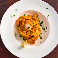 Ein Teller Tagliatelle al Salmone, garniert mit Petersilie und einer Zitronenspalte, daneben ein Glas Weißwein.
