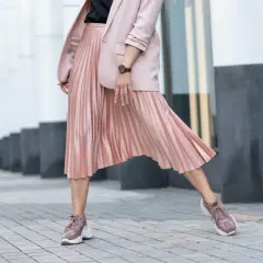 Kobieca stylizacja: pudrowy różowy żakiet i plisowana spódnica. Jakie buty do plisowanej spódnicy? Sneakersy w tym samym kolorze tworzą modny look.
