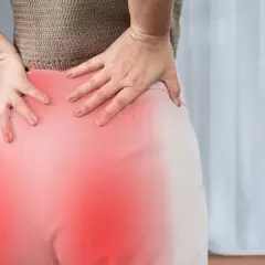 Kobieta trzyma się za bolące biodro, gdzie czerwony obszar sugeruje zapalenie korzonków.