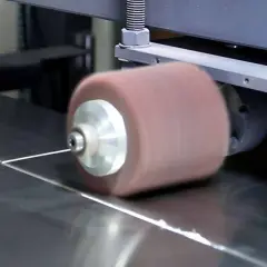 Máquina puliendo acero inoxidable. Un rodillo abrasivo gira sobre una superficie metálica, dejándola brillante.