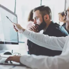 Analityk biznesowy wskazuje na wykres na monitorze, omawiając dane z kolegą.