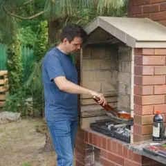 Mężczyzna grilluje mięso w ceglanym piecu. Wnętrze pieca wyłożone jest cegłami szamotowymi, które doskonale utrzymują ciepło.