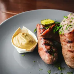 Pyszna kiełbasa szynkowa z piekarnika, podana z musztardą i ogórkiem kiszonym. Idealna na obiad.