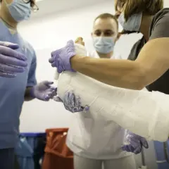 Trzy osoby w maseczkach i rękawiczkach zakładają gips na nogę pacjenta.