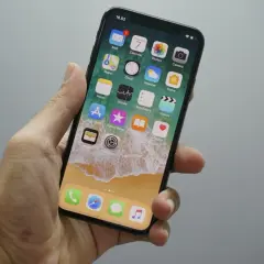 Dłoń trzyma iPhone'a z widocznym ekranem głównym. Chcesz wiedzieć, jak wyłączyć wibracje w iPhone? Wystarczy wejść w Ustawienia.