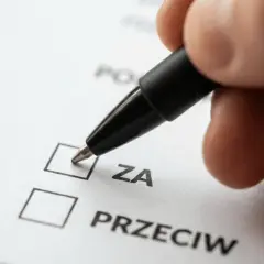 Dłoń z długopisem zaznacza opcję "ZA" na dokumencie. To ważny krok w zwołaniu zebrania wspólnoty mieszkaniowej przez właścicieli lokali.