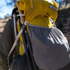 Kijki trekkingowe przymocowane do żółtego plecaka Gossamer Gear. Paski i siatkowa kieszeń pomagają w transporcie.
