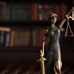 Figurka Temidy z wagą i mieczem na tle biblioteczki. Zastanawiasz się, ile trwa rozprawa karna w sądzie?