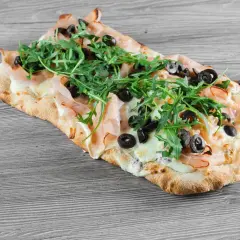 Pinsa co to? Podłużna, chrupiąca baza z szynką, mozzarellą, rukolą i oliwkami. Pyszna alternatywa dla pizzy.