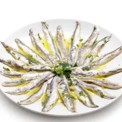 Acciughe al verde disposte a raggiera su un piatto bianco, condite con olio, aglio e prezzemolo.