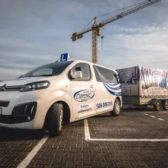 Biały samochód nauki jazdy z literą "L" na dachu i przyczepą z napisem "KAT. B+E" na placu manewrowym.