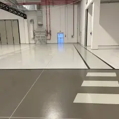 Pavimento industriale con finitura in resina epossidica, segnali di sicurezza e porte a libro.