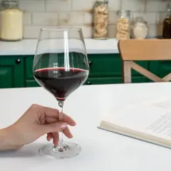 Dłoń trzyma kieliszek czerwonego wina, obok leży otwarta książka. Standardowy kieliszek ma ok. 150 ml.