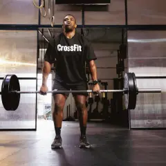 Mężczyzna w koszulce CrossFit podnosi sztangę na siłowni.