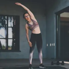 Femme faisant des étirements pour sa séance de musculation maison. Elle est en tenue de sport, bras levé, penchée sur le côté.