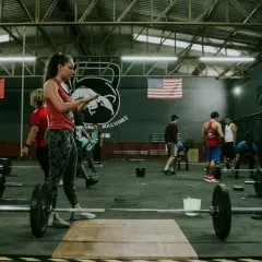 Ludzie ćwiczą w siłowni crossfit. Zastanawiasz się, crossfit po jakim czasie efekty? Widoczni są zawodnicy i sprzęt do treningu.
