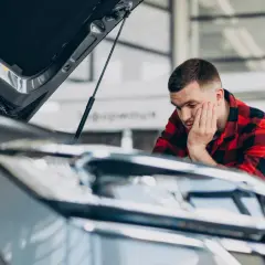 Mężczyzna w kratę sprawdza auto po naprawie bezgotówkowej. Zamyślony, opiera głowę na dłoni.