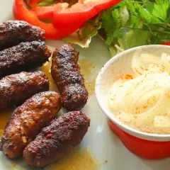 Saftige Cevapcici, frisch zubereitet, liegen auf einem Teller neben Zwiebeln und Salat. Perfekt zum cevapcici selber machen!