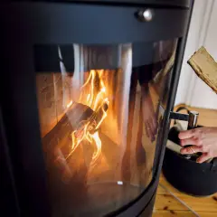 Hände legen Holzscheite in einen modernen Kamin, der brennt. Informieren Sie sich, welche Kamine noch erlaubt sind.