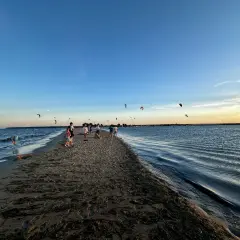 Ludzie spacerują po piaszczystym cyplu Rewskim, gdzie można podziwiać kitesurferów. Jak dojechać? To proste, wystarczy kierować się nad morze.