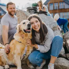 Uśmiechnięta rodzina z psem na tle drewnianych domków. Czy na Śnieżkę można z psem? Tak, jeśli jest tak szczęśliwy jak ten złoty retriever!