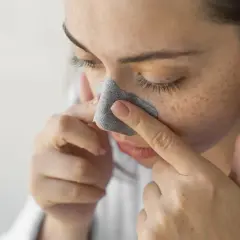Kobieta z piegami stosuje plaster na nos, szukając domowych sposobów, jak usunąć wągry z nosa.