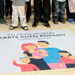Na macie z napisem "Tu honorujemy Kartę Dużej Rodziny" widnieje rysunek rodziny. Dzieci i dorośli stoją wokół.