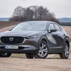 Szary Mazda CX-30 na polnej drodze. Wady tego modelu to m.in. ograniczona widoczność i twarde zawieszenie.
