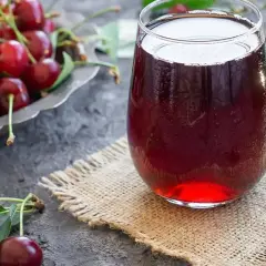 Szklanka orzeźwiającego soku z wiśni, obok miseczki pełnej świeżych owoców. Idealny na lato, prosty sok z wiśni przepis.