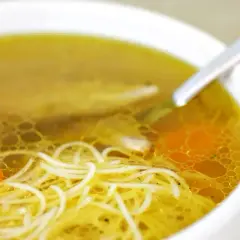 Zbliżenie na miskę z gorącym rosołem z makaronem i kawałkami marchewki.